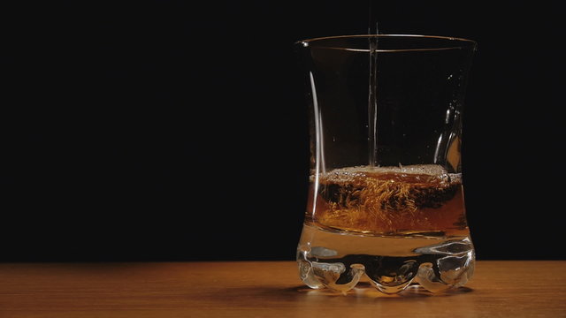 Liquor or whiskey poured in a glass against black background