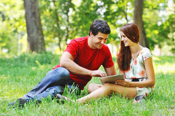 Couple relaxing together in summer park with tablet computer pc