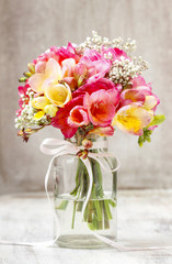 Bouquet of colorful freesia flowers in transparent glass vase.