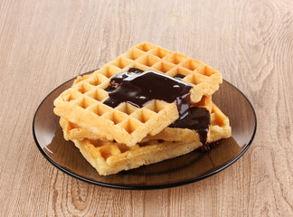 Tasty waffles with chocolate on plate on wooden background