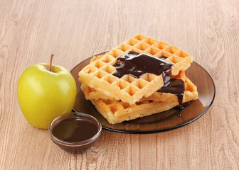 Tasty waffles with chocolate on plate on wooden background