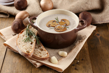 Mushroom soup in pot, on wooden background
