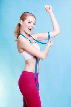 Fitness girl sporty woman measuring her biseps on blue