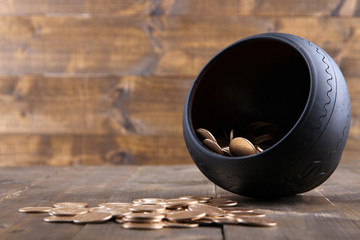 Golden coins falling out from pot, on wooden background
