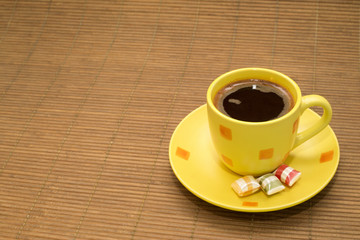 Yellow cup of coffee and a colorful candies on wooden rug
