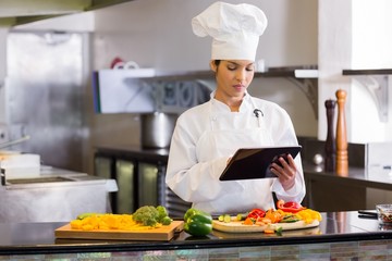 Female chef using digital tablet while cutting vegetables