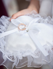 Closeup shot of witness holding white cushion with wedding rings