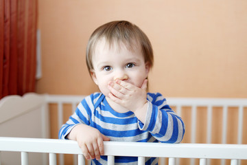 baby keeps silent standing in white bed