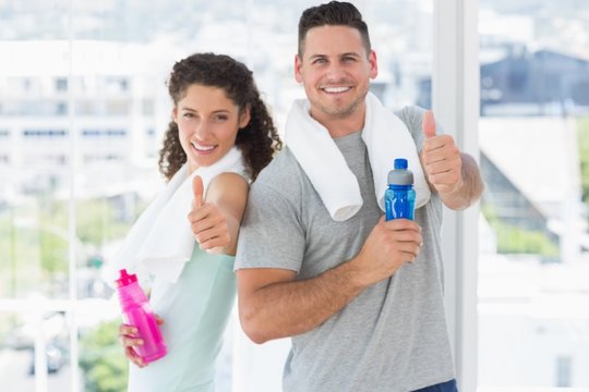 Couple with water bottles gesturing thumbs up at gym