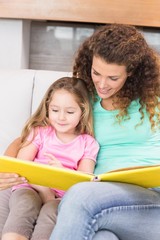 Obraz premium Pretty mother helping her little daughter read a storybook