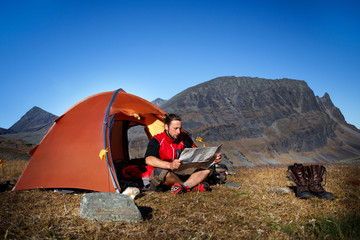 Hiker in front of his Tent, looking Map