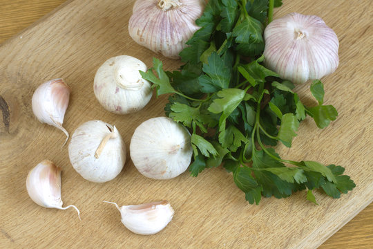 Ripe garlic and green parsley on wooden cutting board