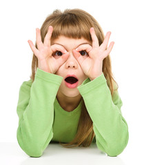 Astonished little girl is showing glasses gesture