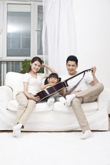 .Young family playing guitar in living room.