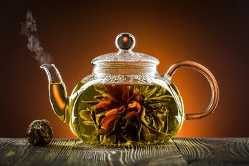 Photo sur Plexiglas Theé Théière en verre avec fleur de thé en fleurs sur table en bois