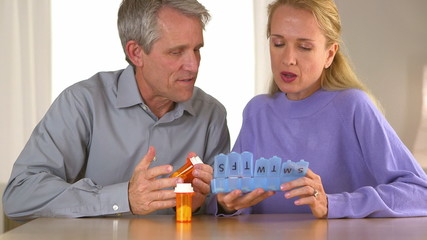 Mature couple putting pills in box - Powered by Adobe