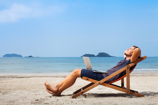 happy business man with laptop relaxing on the beach