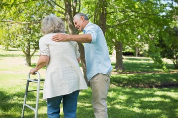 Mature man assisting woman with walker at park