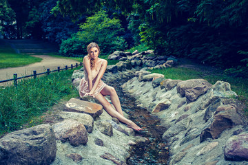 Fototapeta premium Gorgeous woman sitting on rock by stream in park
