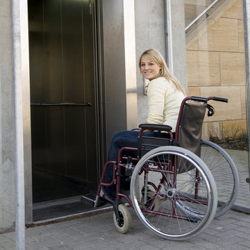 Frau in Rollstuhl fährt in Fahrstuhl