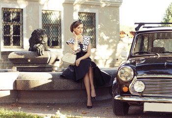 A sexy woman sitting next to a retro car on the street