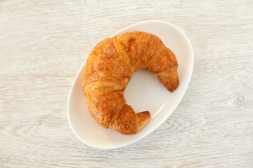 One croissant on a white plate on wooden surface