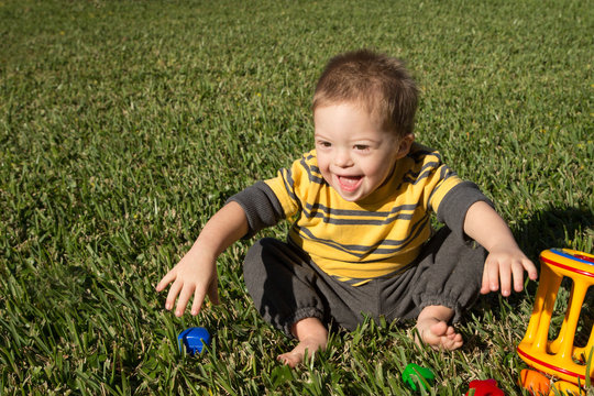 Laughing Down Syndrome child in grass with toys