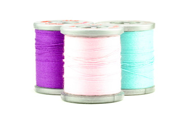 Three spools of purple, pink, and light blue thread, on white