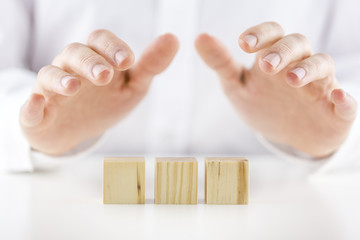Man holding protective hands above three wooden cubes