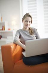 beautiful young woman sits on sofa and using laptop