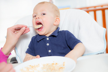 Mother feeding hungry baby in the highchair indoors