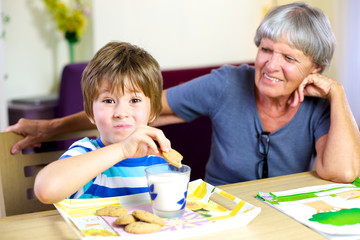 Fototapeta premium Szczęśliwe dziecko o przekąskę podczas pracy domowej z uśmiechniętą babcią