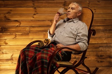 Senior man with smoking pipe sitting on rocking chair