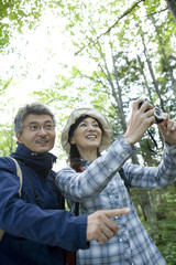 senior husband and wife taking photograph in greenery