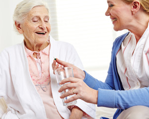 Seniorin nimmt Tablette mit Wasser
