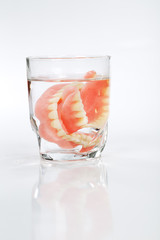 A set of dentures in a glass of water on a white background