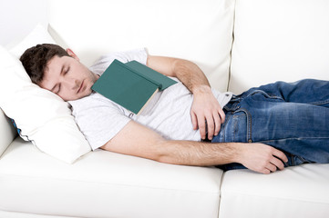 Fototapeta premium tired young man sleeping on couch with book on lap