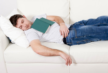 tired young man sleeping on couch with book on lap