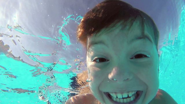 Cute teen boy dives in blue pool with open eyes