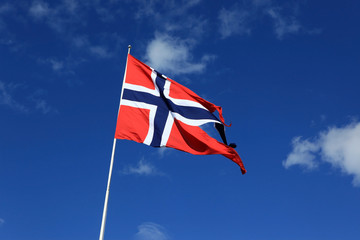 A Norwegian flag blowing in the wind against blue sky with cloud