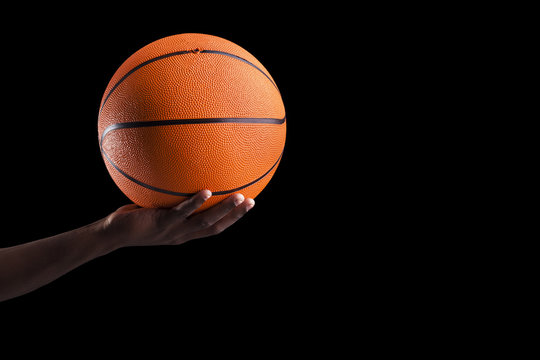 Basketball player holding a ball against dark background