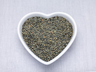 Green lentils in a heart shaped bowl on a woven table cloth