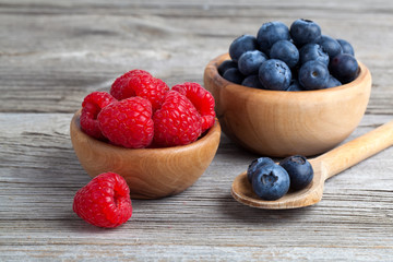 Blueberry and raspberries in bowls on wooden background