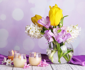 Flowers in vase with candles on table on bright background