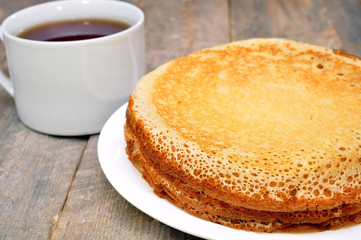 pancakes on a plate on a wooden table and a cup of tea