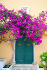 Greek monastery door with beautiful purple flowers - 62102324