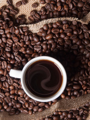 white cup with coffee on burlap background with beans