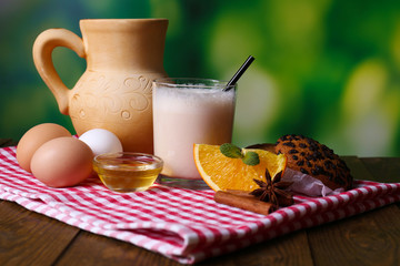 Eggnog with milk and eggs on tablecloth on natural background
