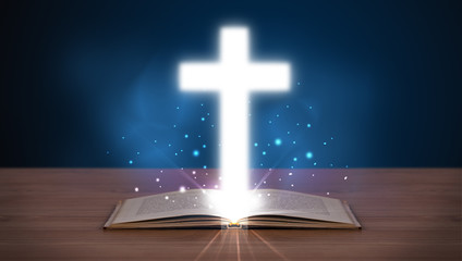 Open holy bible with glowing cross in the middle