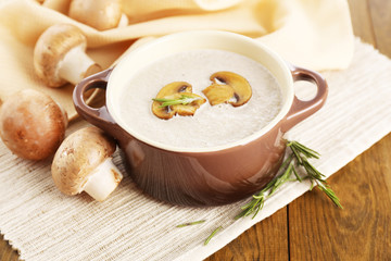 Mushroom soup in pot, on wooden background